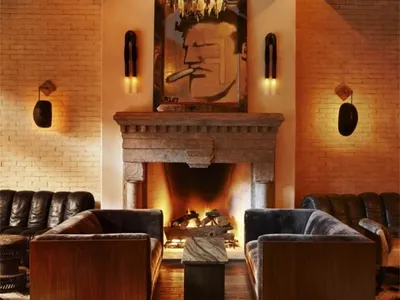 A cozy industrial-style living room with brick walls, wooden beams, and a stone fireplace.