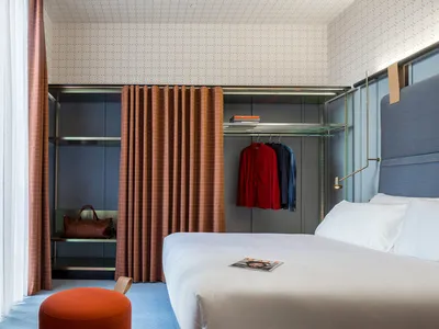 Modern minimalist bedroom with blue carpet, orange pouf, and organized closet