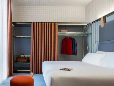 A minimalist bedroom with a bed, ottoman, and open closet