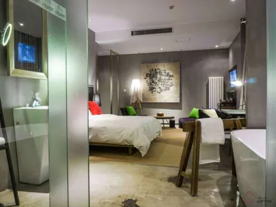 A modern minimalist bedroom with a white bed, green accents, and abstract wall art.