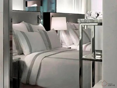 A minimalist bedroom with white-on-white striped bedding and a sleek, modern headboard and bedside table.