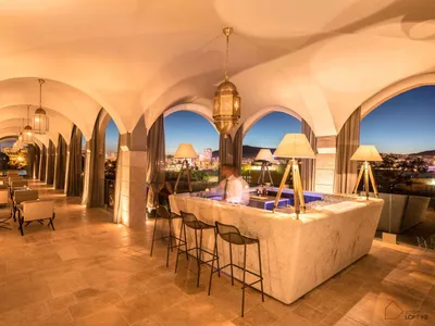 Modern bar interior with marble furniture and seating, overlooking a cityscape.