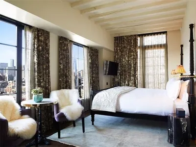 Modern bedroom featuring a bed with white linens, a fur-covered accent chair, and floral arrangement on a small round table w