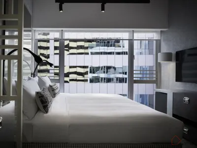 Clean, modern bedroom with a minimalist aesthetic, featuring a sleek bed with white bedding, and a large window offering city