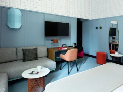 A modern hotel suite featuring a comfortable sofa, a flat-screen TV, a desk with a chair, and a coffee table with a magazine