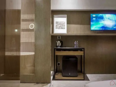 A modern minimalist hotel room with wooden accents, glass partitions, and metallic furniture.