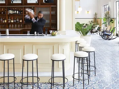 A modern restaurant bar with white floor tiles and a bartender preparing drinks.