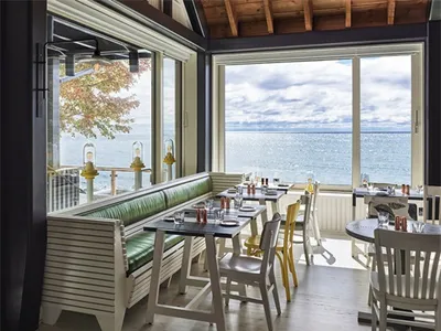 A modern restaurant with a sea view, featuring wooden furniture and large windows.