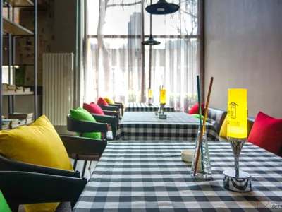 A modern restaurant setting with a black and white checkered tablecloth, colorful cushions, and a warm yellow table lamp.