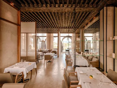 Modern restaurant interior with industrial-style decor featuring wooden ceiling, glass shelves, and concrete flooring.