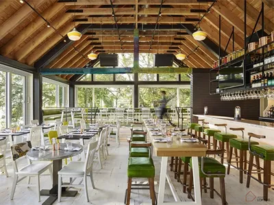 A modern restaurant interior with wooden tables, chairs, and bar stools.