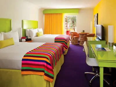 A brightly colored hotel room with colorful textiles, two beds, and yellow and purple accents.