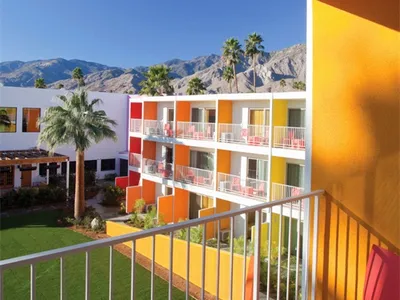 Hotel room balcony with metal railing, concrete floor, and glass wall overlooking palm trees and mountains.