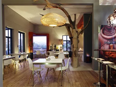 A modern industrial-style restaurant with wooden tables, metal bar stools, and glass windows.