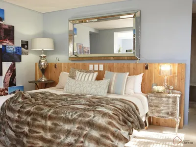 A modern bedroom with a bed covered in a plush fur blanket, framed photographs on the wall, and a wooden headboard.