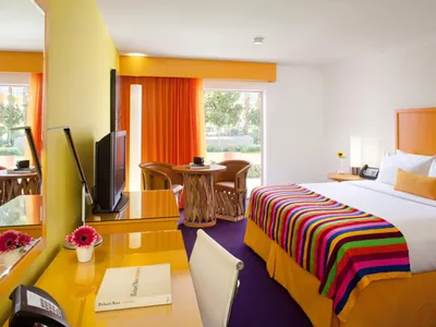 A modern hotel room featuring a bed with a colorful striped blanket, a wooden table, and various decor items.