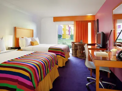 A modern hotel room with two beds, colorful striped bedding, and a warm, welcoming atmosphere.