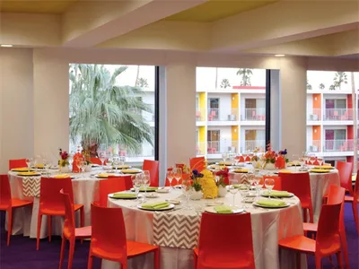A lively, modern hotel ballroom with red chairs and white tablecloths