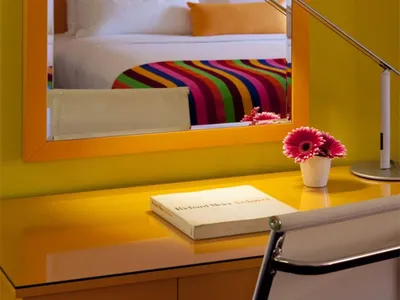 A modern bedroom with yellow furniture, a colorful striped blanket, and a white chair.