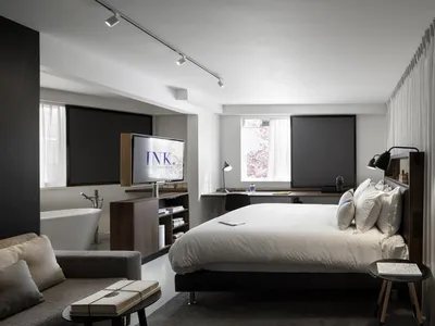 A modern minimalist hotel room with a bed, sofa, bathtub, and television.