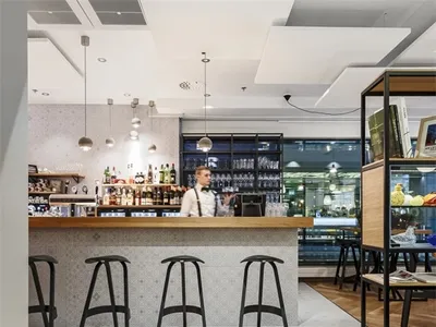 Interior design of a modern bar with wooden flooring, concrete walls, and glass elements.