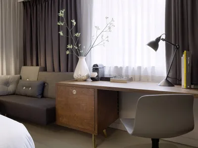 Modern, minimalist home office with a wooden desk, white vase with greenery, and black desk lamp.