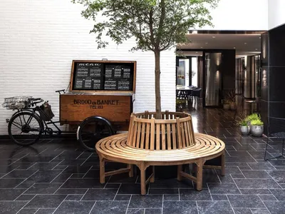 Modern interior of a restaurant with wooden seating, cement floors, and potted plants for decoration.