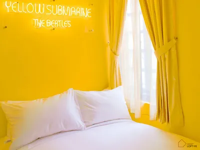 A minimalist bedroom with yellow walls, a white bed, and yellow curtains.