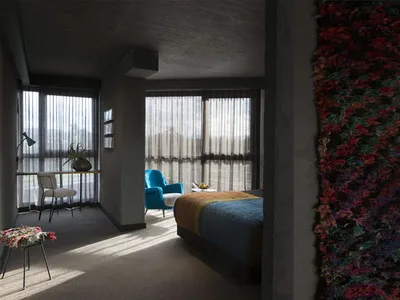 A modern bedroom featuring a concrete wall with embedded hyphae, a blue armchair, and a desk with a plant.