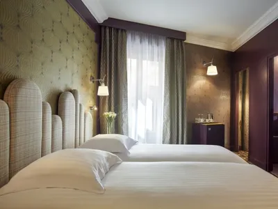 A modern bedroom featuring a twin bed with white bedding, white headboard, and a window with curtains and a vase of flowers.