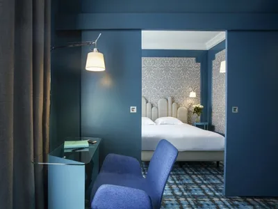 A modern hotel room with blue walls, fabric headboard, and glass desk.