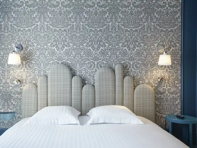 Modern hotel room featuring a textured wallpaper and upholstered bed with white pillows and lamps.