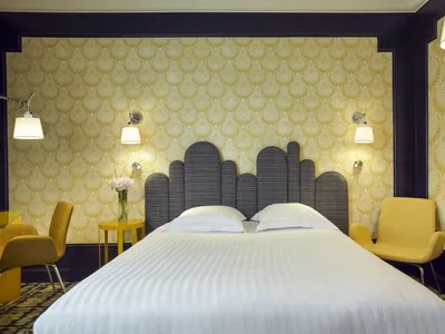 Modern bedroom featuring a double bed adorned with white bedding against a bold yellow patterned wallpaper backdrop.