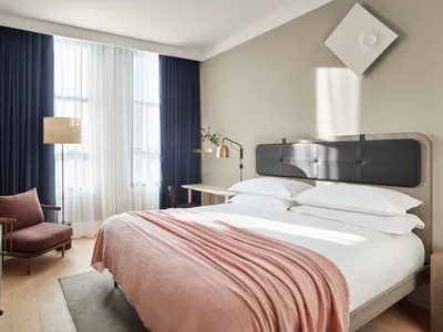 A minimalist bedroom with a double bed, pink blanket, and desk with lamp.