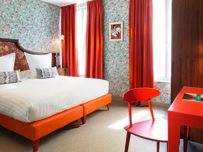 A minimalist bedroom featuring bright orange furniture and red-orange patterned curtains with a framed picture on the wall.