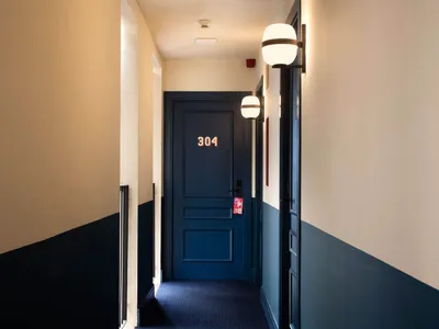 A minimalist hotel room with blue and white painted walls, featuring a numbered door and hallway lighting.