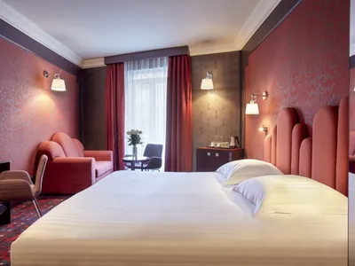 Modern hotel room with a bed, armchair, sofa, and coffee table.