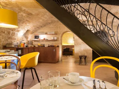 Modern cafe interior with wooden stairs, yellow chairs, and a rustic stone wall