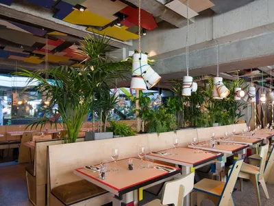 A modern industrial restaurant interior featuring concrete floors, wooden furniture, and green plants.