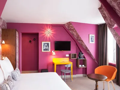 A modern hotel room with a prominent pink wall, white bed, and yellow desk.