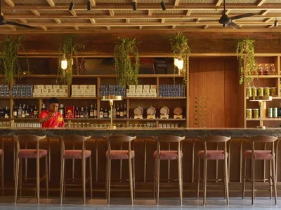A modern industrial restaurant bar with wooden seating, glass shelves, and metal fans.