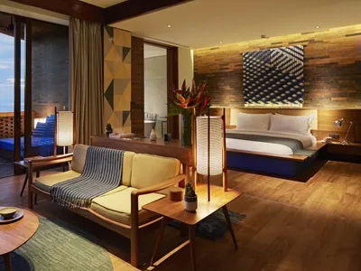 A modern resort bedroom suite featuring a wooden sofa, concrete flooring, and a view of the ocean.