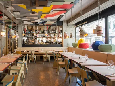 Modern restaurant interior with colorful geometric shapes, concrete and wood materials, and industrial design elements.