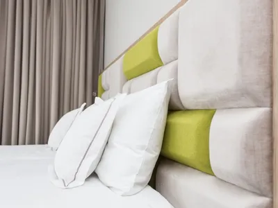 A minimalist bedroom with a fabric headboard featuring green accents and white pillows.