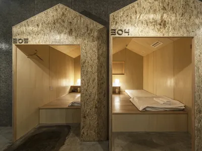 A minimalist bedroom with wooden walls, a single bed, and simple lighting fixtures.