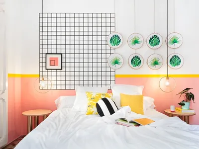A modern bedroom with a white bed, vibrant accents, and geometric grid design on the wall.