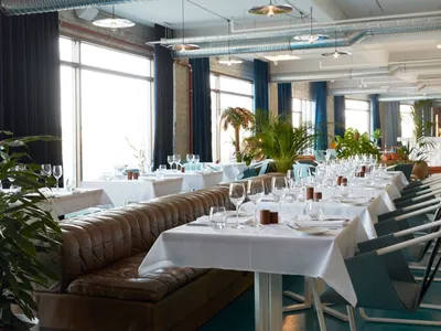 A modern restaurant interior filled with green plants and white tables.