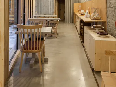 A spacious, industrial-style restaurant interior featuring concrete walls, wooden tables, and chairs.