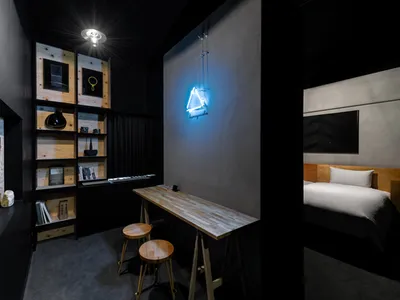 A minimalist bedroom with a wooden headboard and a wooden table in front of a wall mounted with books and decorative objects.