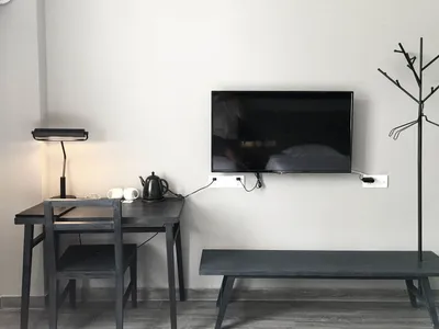 A minimalistic hotel room with a black desk, black bench, and a mounted television on the wall.